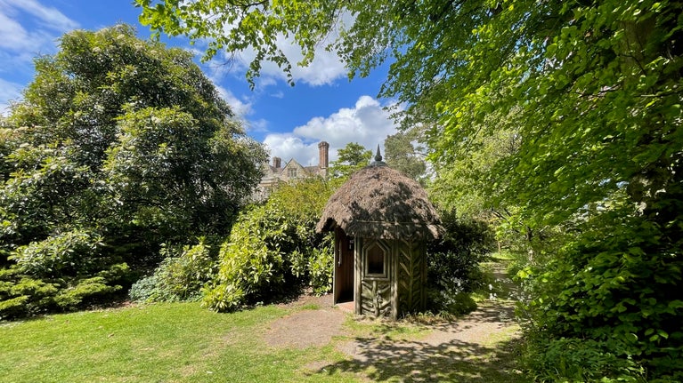Glimpse of a manor house above a thatched garden summer house